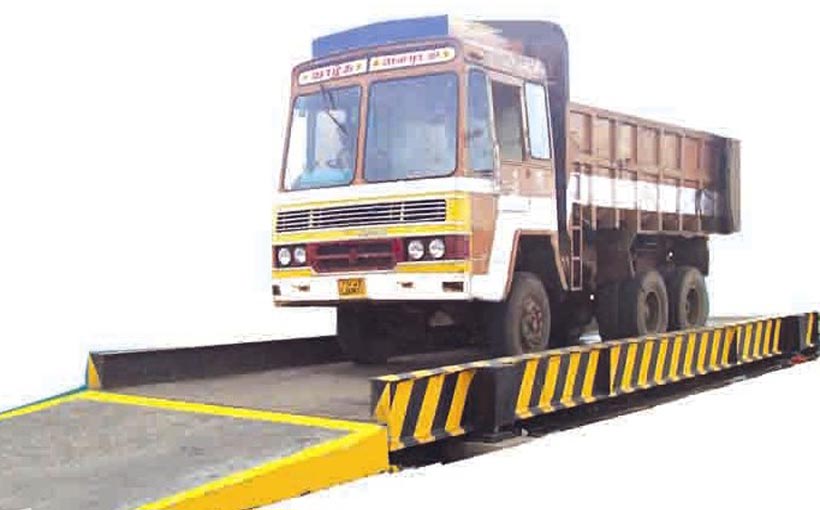 Truck on a pitless weighbridge with safety barriers on both sides for weight measurement.